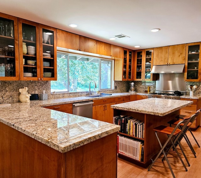 kitchen featuring a kitchen island, a breakfast bar, sink, stainless steel dishwasher, and light stone countertops