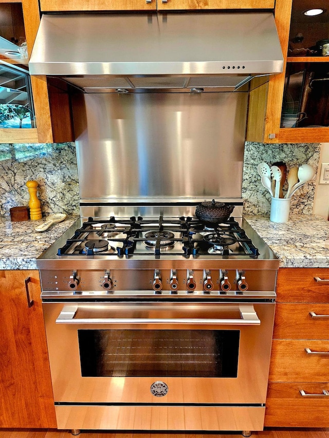 kitchen with decorative backsplash, light stone countertops, exhaust hood, and high end stainless steel range oven