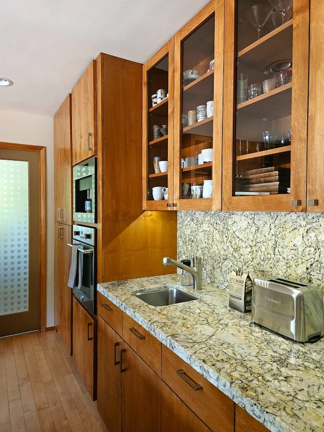 kitchen featuring tasteful backsplash, sink, oven, light stone countertops, and light hardwood / wood-style flooring