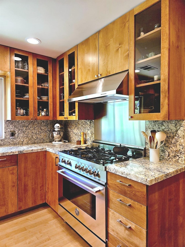 kitchen featuring light stone counters, high end range, tasteful backsplash, and light wood-type flooring