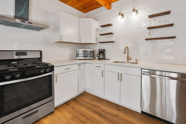 kitchen with appliances with stainless steel finishes, white cabinets, wall chimney range hood, sink, and light hardwood / wood-style floors