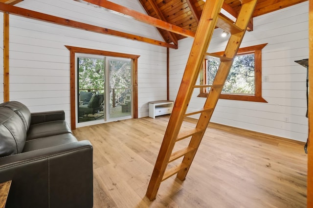 living room with vaulted ceiling with beams, wood walls, and light hardwood / wood-style floors