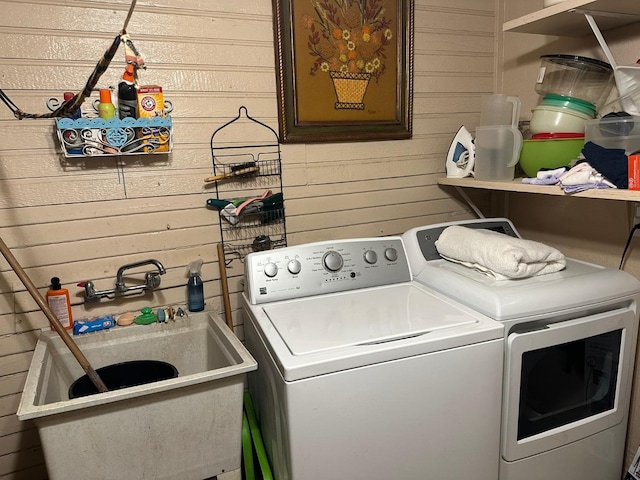 laundry area featuring wood walls, independent washer and dryer, and sink