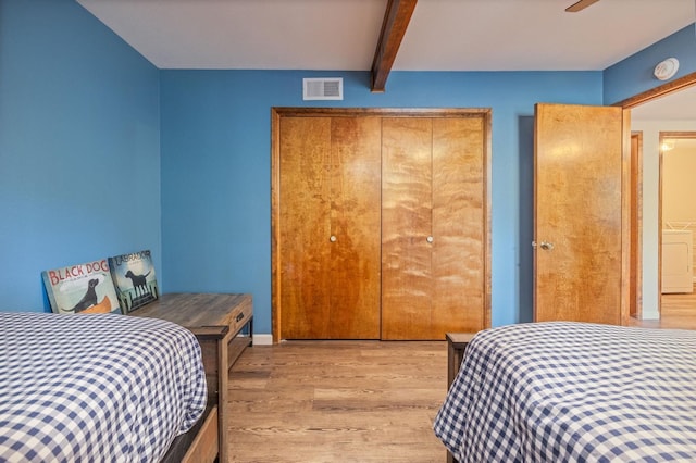 bedroom with beamed ceiling, washer / clothes dryer, ceiling fan, light hardwood / wood-style floors, and a closet