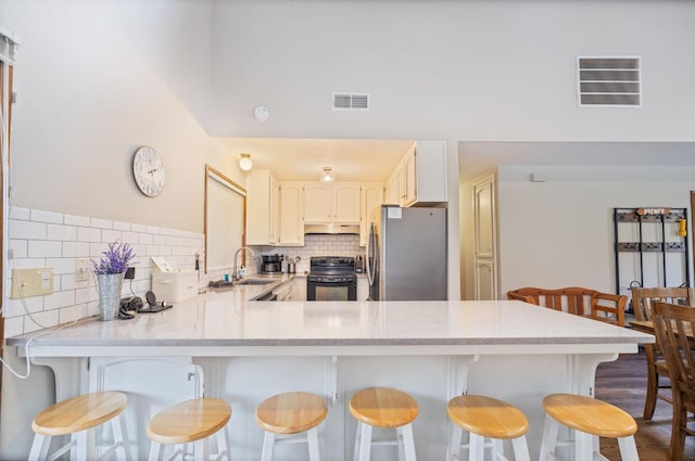 kitchen featuring a breakfast bar, sink, stainless steel fridge, kitchen peninsula, and black range with electric stovetop