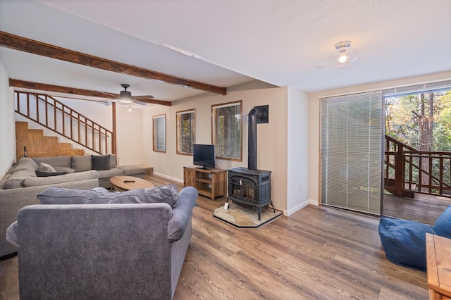 living room featuring hardwood / wood-style floors, beamed ceiling, a wood stove, ceiling fan, and a textured ceiling