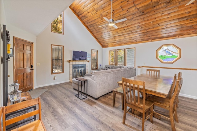 dining space with ceiling fan, hardwood / wood-style floors, high vaulted ceiling, a tiled fireplace, and wooden ceiling