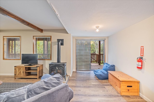 living room with a textured ceiling, a wood stove, beamed ceiling, and light wood-type flooring