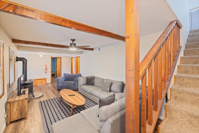 living room featuring beam ceiling, ceiling fan, a wood stove, and light hardwood / wood-style floors