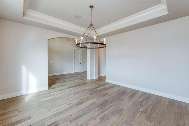 unfurnished dining area with arched walkways, a tray ceiling, and light wood finished floors