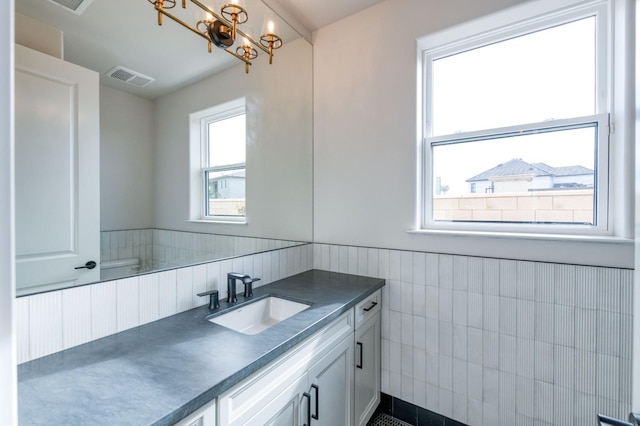 bathroom with a chandelier, vanity, visible vents, tile walls, and wainscoting