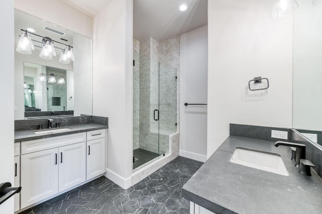 full bath with a stall shower, two vanities, a sink, and baseboards