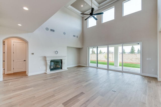 unfurnished living room featuring light wood-type flooring, a glass covered fireplace, visible vents, and arched walkways