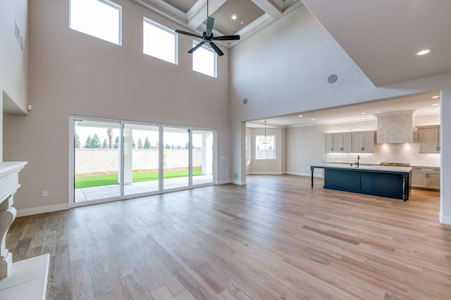 unfurnished living room featuring baseboards, a ceiling fan, light wood-style flooring, crown molding, and a sink