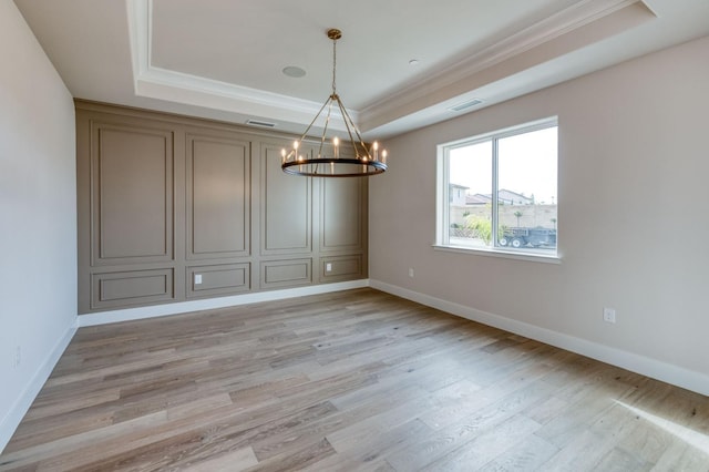 unfurnished room featuring a raised ceiling, light wood-style flooring, an inviting chandelier, ornamental molding, and baseboards