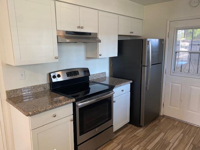 kitchen with appliances with stainless steel finishes, white cabinetry, dark stone counters, and wood-type flooring