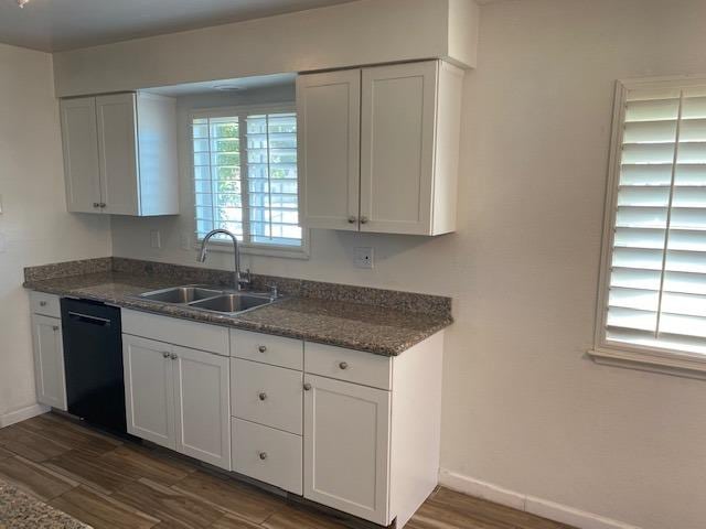 kitchen with black dishwasher, dark wood-type flooring, white cabinetry, dark stone countertops, and sink