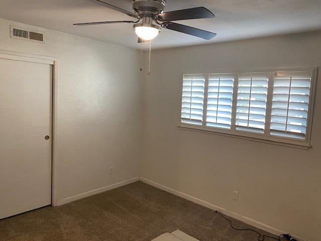 spare room featuring dark carpet, ceiling fan, and a healthy amount of sunlight