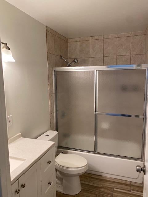 full bathroom featuring toilet, vanity, shower / bath combination with glass door, and hardwood / wood-style flooring