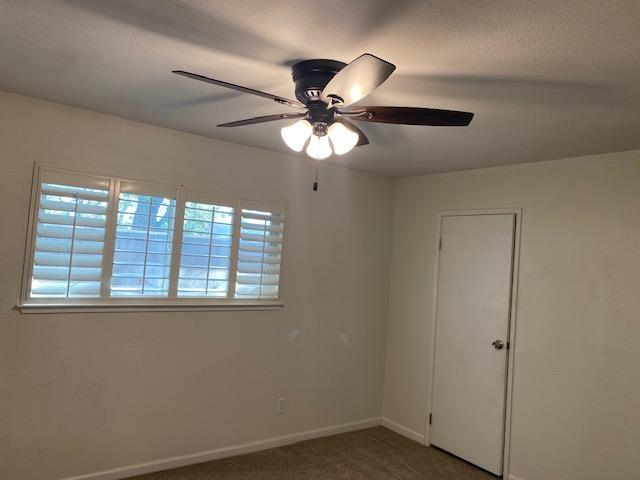 unfurnished room featuring dark carpet, ceiling fan, and a wealth of natural light