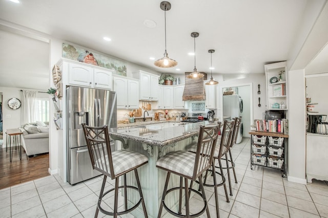 kitchen with stainless steel refrigerator with ice dispenser, light stone counters, white cabinetry, light tile patterned floors, and stove