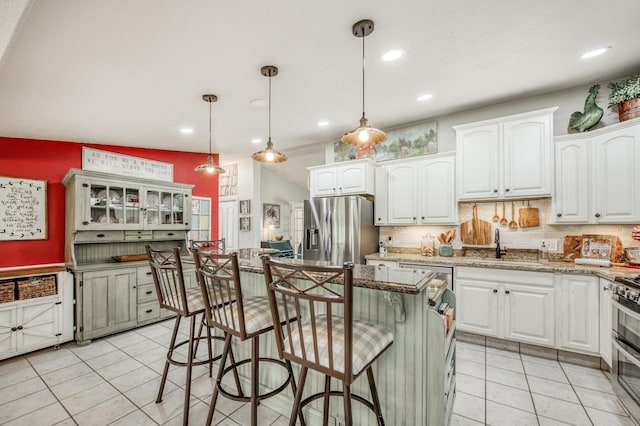 kitchen with a kitchen island, a breakfast bar area, light tile patterned floors, stainless steel appliances, and white cabinetry