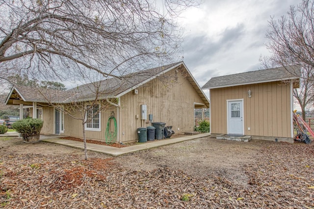 rear view of house featuring an outbuilding and roof with shingles