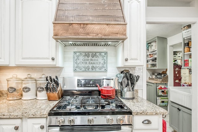 kitchen featuring premium range hood, gas range, backsplash, and white cabinets