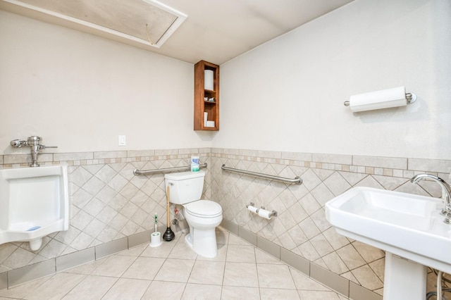 half bath with a sink, tile patterned flooring, wainscoting, tile walls, and toilet
