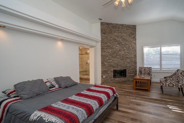 bedroom with a stone fireplace, vaulted ceiling, ceiling fan, connected bathroom, and wood-type flooring