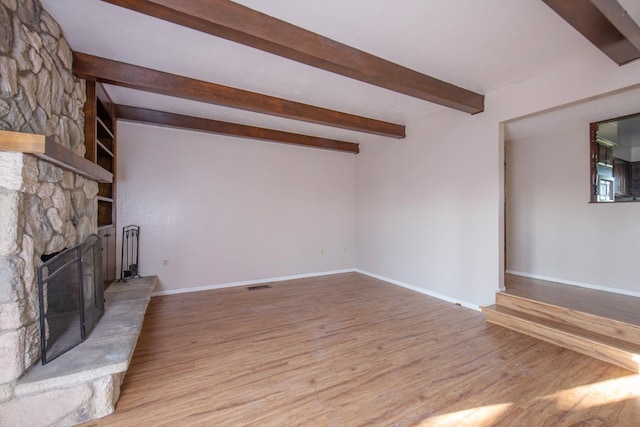 unfurnished living room featuring beamed ceiling, light hardwood / wood-style floors, and a fireplace