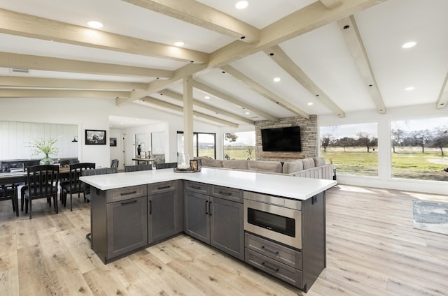 kitchen featuring a kitchen island, vaulted ceiling with beams, stainless steel microwave, and light wood-type flooring