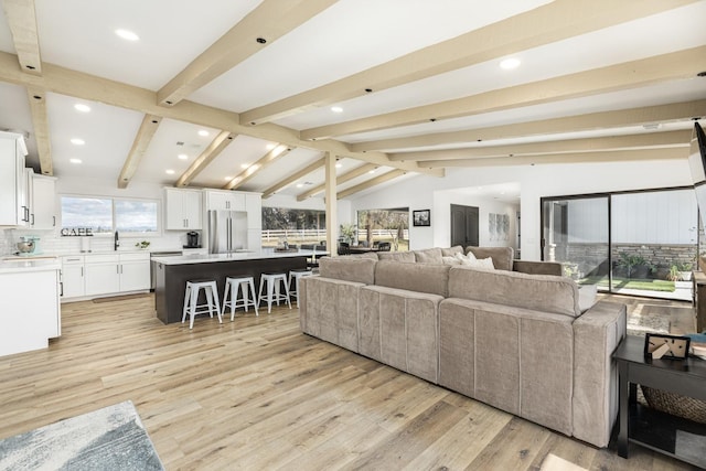 living room featuring lofted ceiling with beams, sink, and light hardwood / wood-style floors