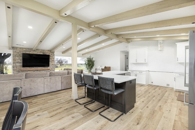 kitchen with a kitchen bar, vaulted ceiling with beams, white cabinetry, a center island, and light hardwood / wood-style flooring