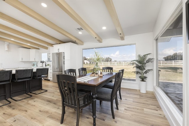 dining area with beamed ceiling, sink, and light hardwood / wood-style flooring