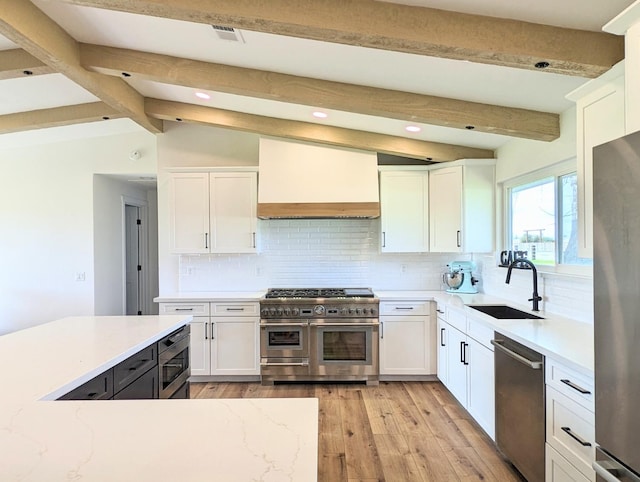 kitchen with sink, custom exhaust hood, white cabinetry, light wood-type flooring, and appliances with stainless steel finishes