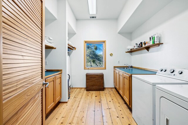 laundry room featuring sink, light hardwood / wood-style floors, cabinets, and washer and clothes dryer