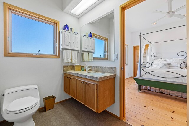 bathroom with wood-type flooring, ceiling fan, vanity with extensive cabinet space, and toilet