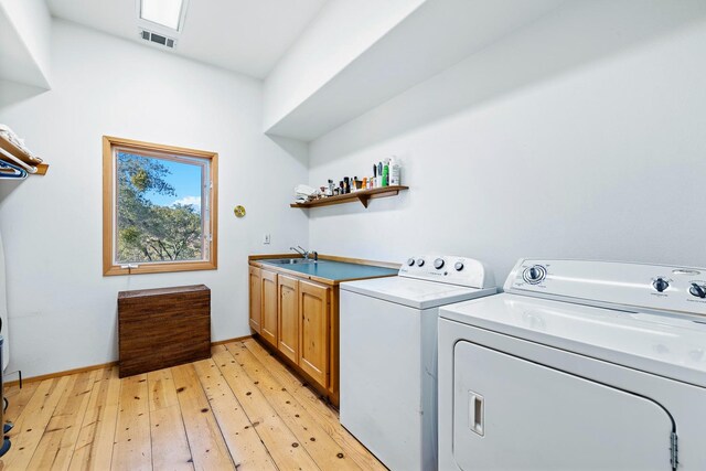 clothes washing area with washing machine and dryer, cabinets, sink, and light wood-type flooring