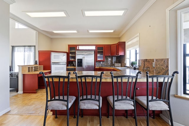 kitchen with kitchen peninsula, white appliances, sink, tasteful backsplash, and ornamental molding