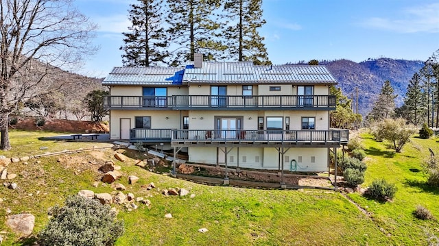 back of property with a lawn, a balcony, and a mountain view