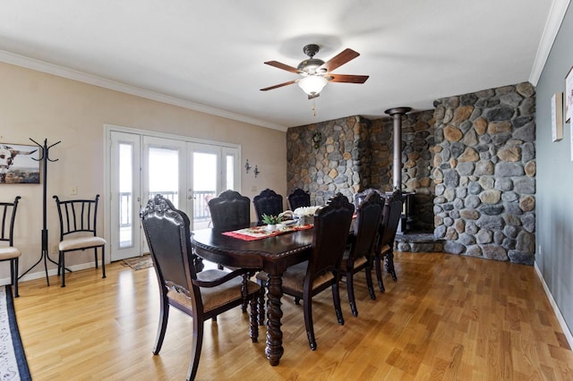 dining area featuring ceiling fan, french doors, light hardwood / wood-style flooring, crown molding, and a wood stove