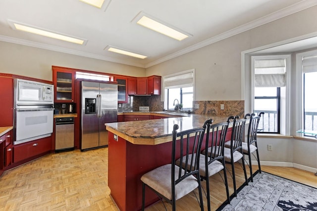 kitchen featuring kitchen peninsula, white appliances, backsplash, a breakfast bar area, and light parquet flooring