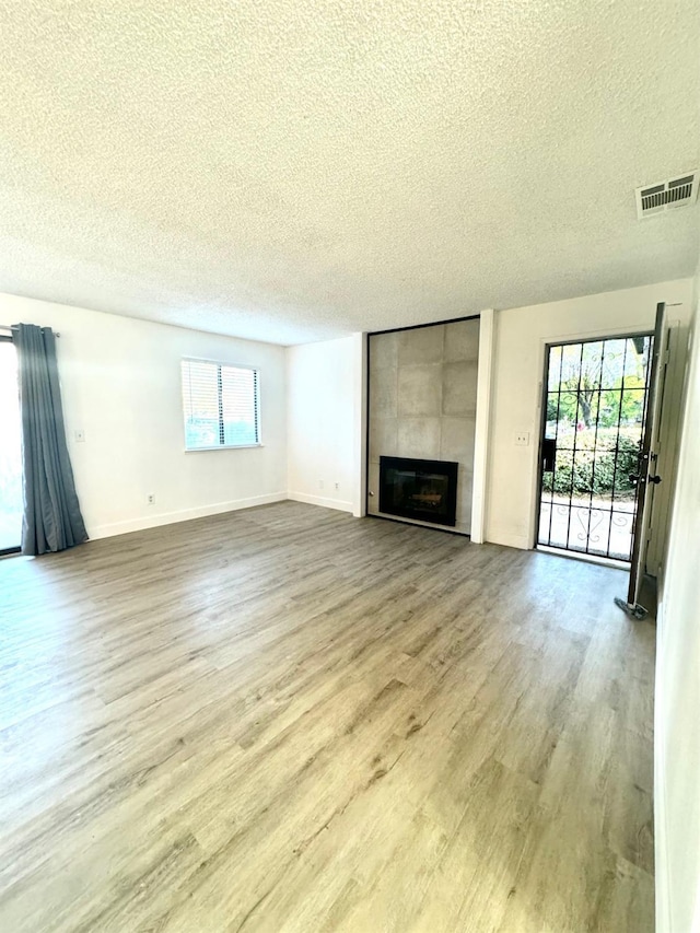 unfurnished living room featuring a tile fireplace, a textured ceiling, light hardwood / wood-style flooring, and a wealth of natural light