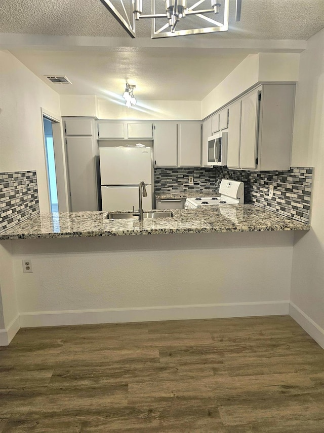 kitchen with white appliances, sink, tasteful backsplash, light stone counters, and kitchen peninsula