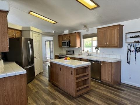 kitchen with a center island, stainless steel appliances, dark hardwood / wood-style flooring, and tile countertops