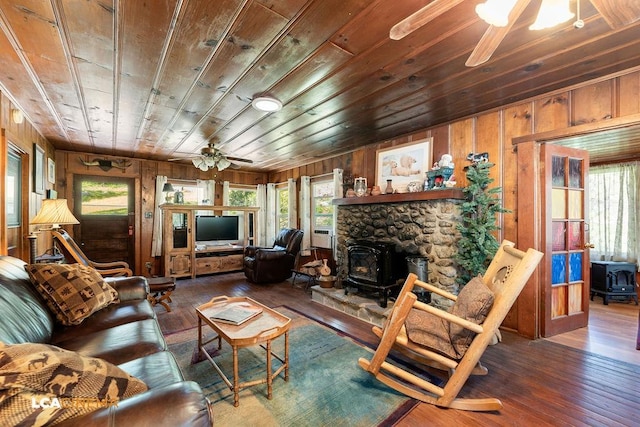 living room featuring ceiling fan, dark hardwood / wood-style floors, wooden ceiling, wood walls, and a wood stove