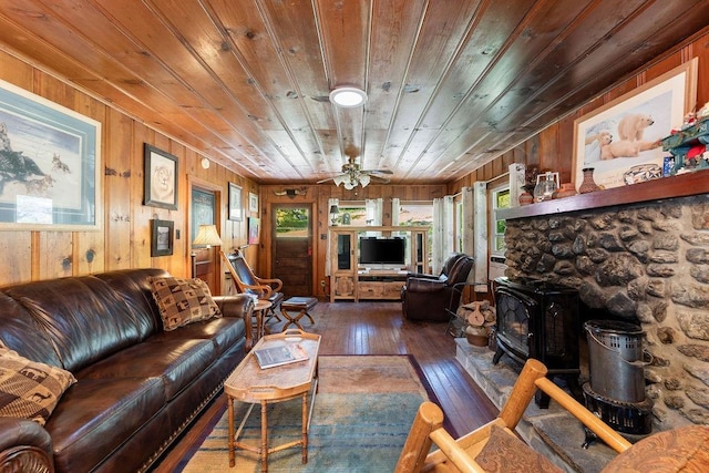 living room featuring wooden walls, a wood stove, dark hardwood / wood-style flooring, wood ceiling, and ceiling fan