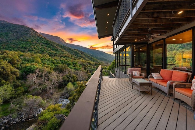 deck at dusk with ceiling fan, an outdoor living space, and a mountain view