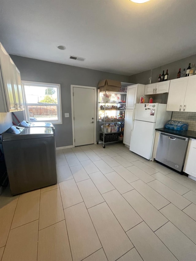 kitchen with stainless steel dishwasher, white fridge, washer / dryer, and white cabinetry